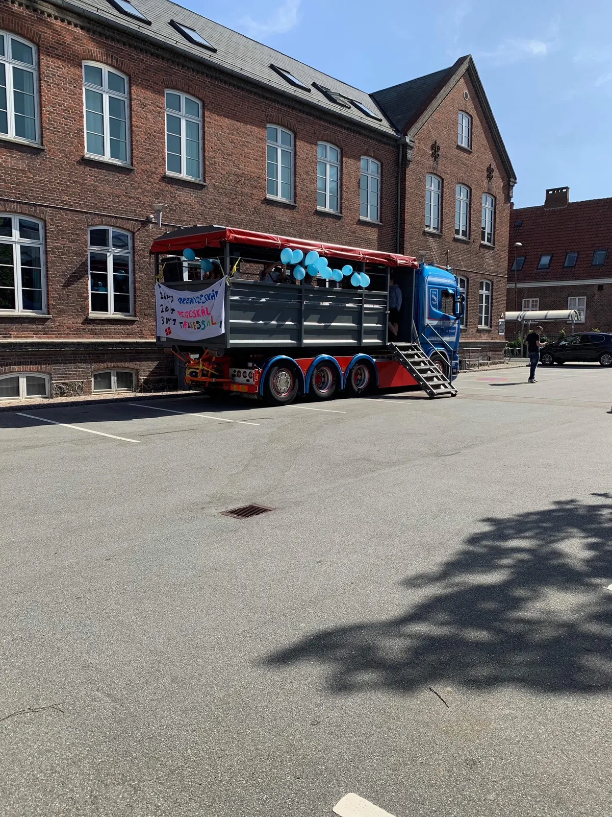 Blå Scania-studentervogn fra VSN Gruppen holder ved skole i solskin